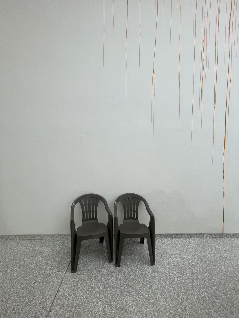 Two dark grey armchairs against a white wall with orange paint drips