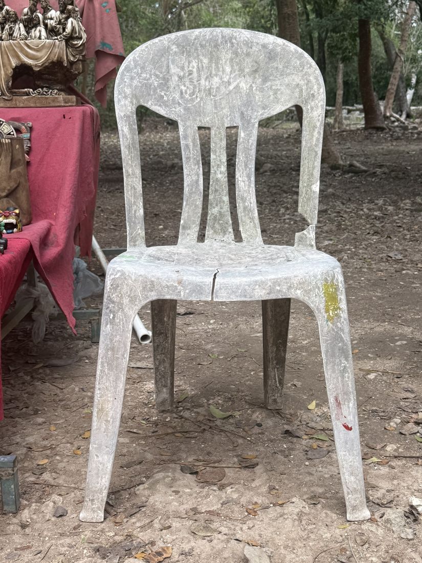 A grey side chair, cracked across the seat, beside a market stall