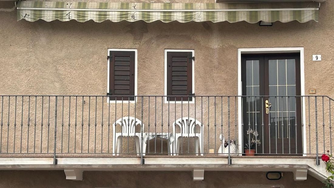 Two white chairs and a small table on a balcony behind iron railings