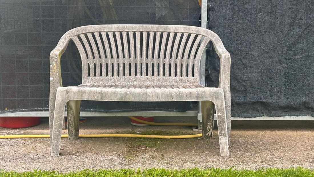 A two-seater plastic bench, grey with moss and age