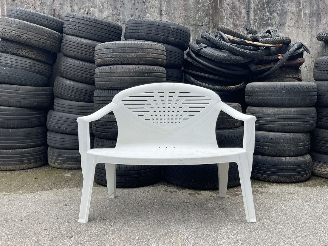 A white two-seater bench in front of piles of old tyres