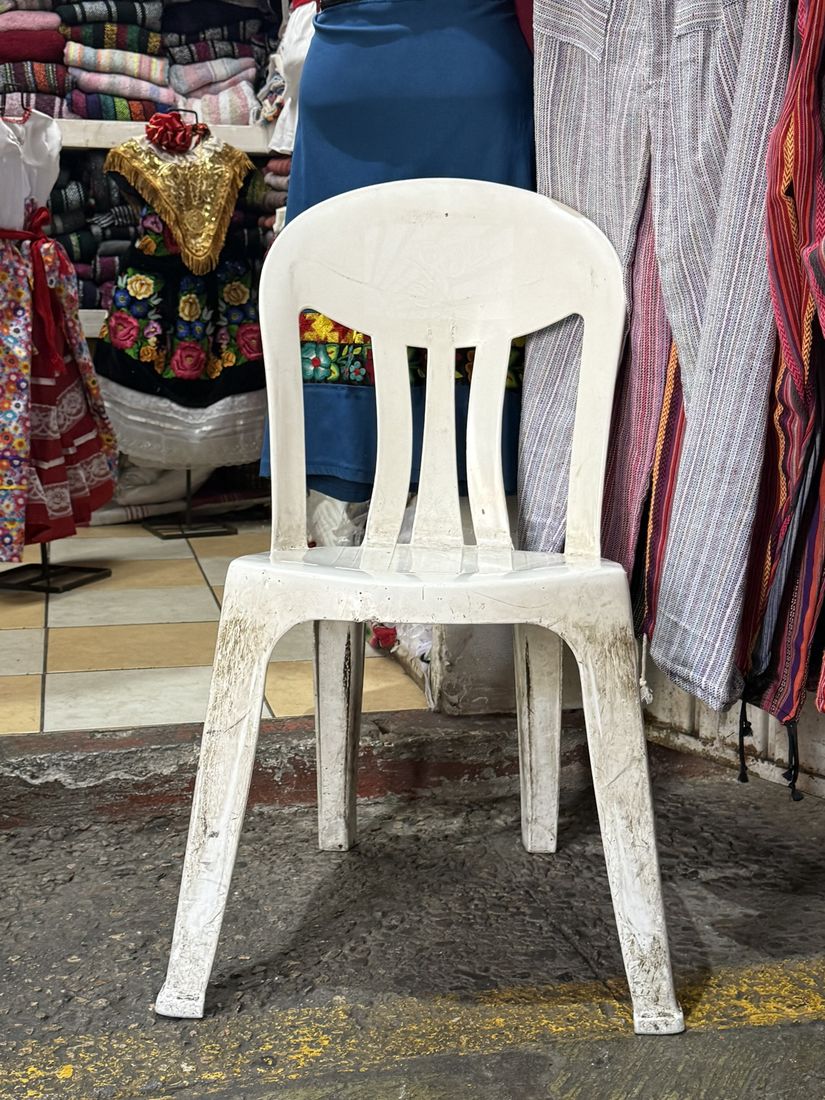 A white side chair in a market among embroidered dresses and woven cloth